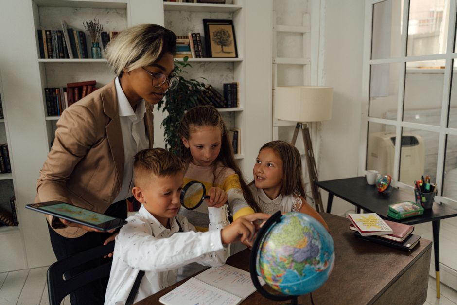 A teacher assists students in learning geography with a globe in a classroom setting.